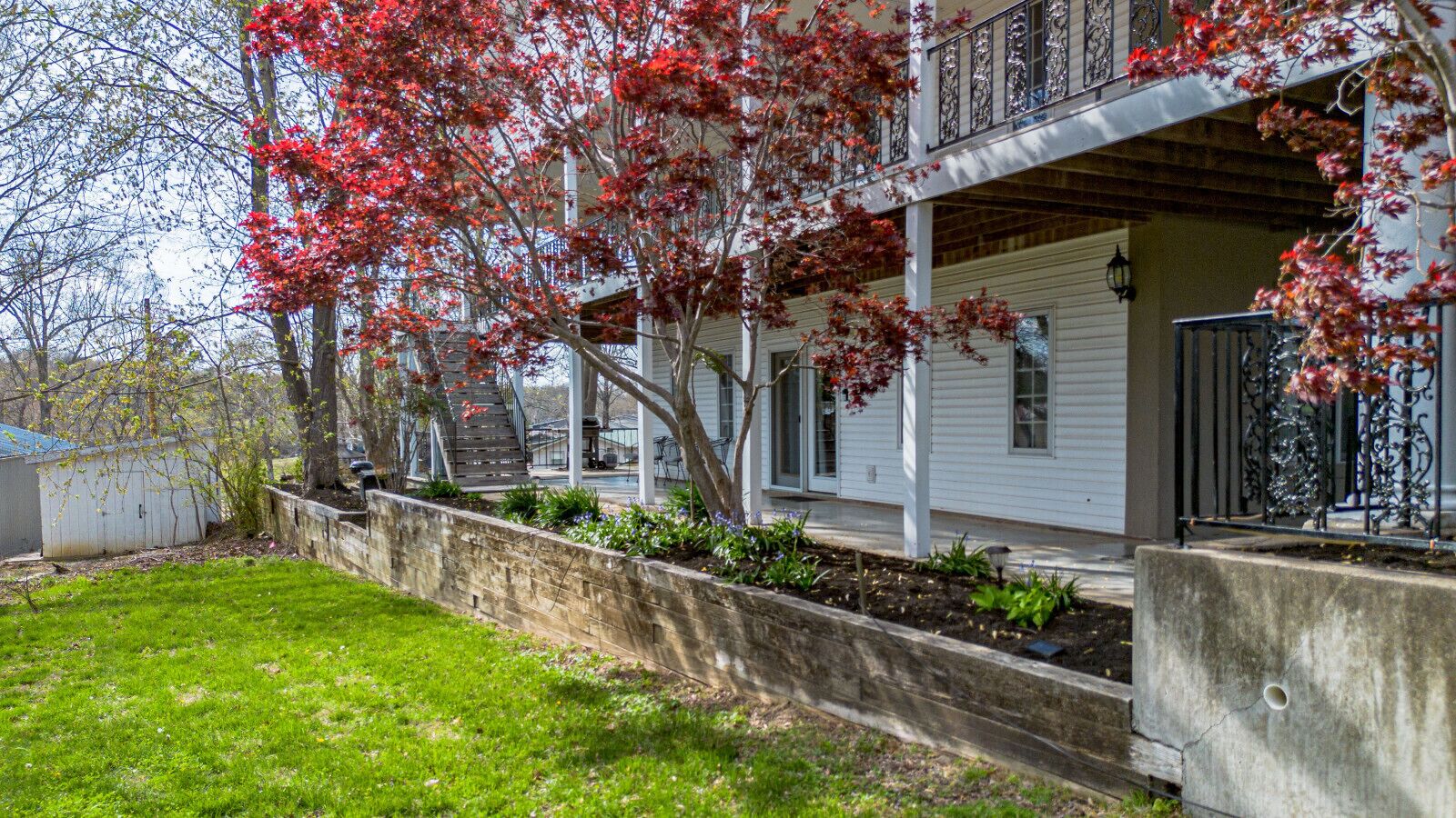 A two-story house with a covered porch, a stone retaining wall, and a small shed in the yard.