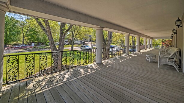 A covered wooden deck with white wicker furniture and a metal railing.