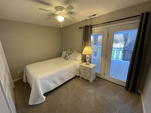 Ein Schlafzimmer mit Bett, Nachttisch, Lampe und Blick ins Freie durch eine Schiebetür.