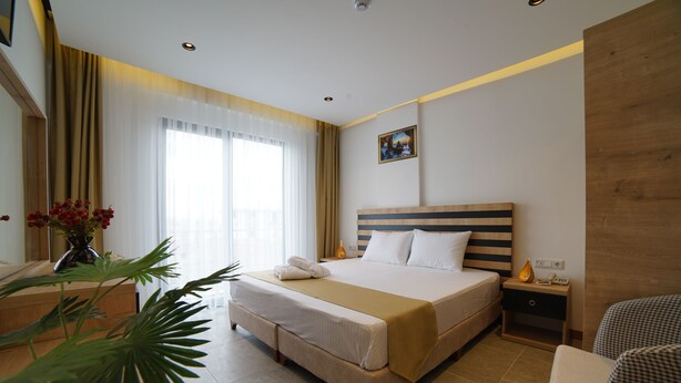 A hotel room with a large bed, bedside tables, a chair, and a potted plant. - ŞAHİN TERMAL OTEL VE SPA (Kutahya)