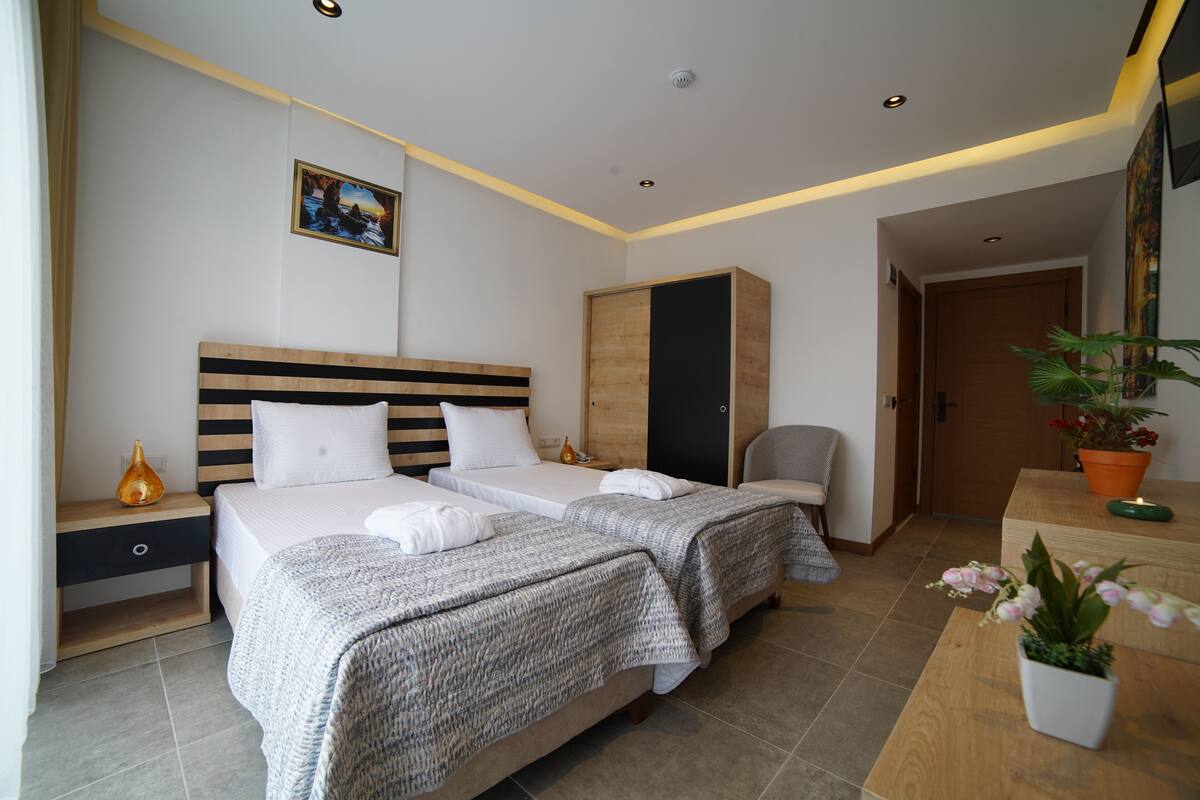 A hotel room with two beds, a wardrobe, a desk with a plant, and a painting on the wall.
