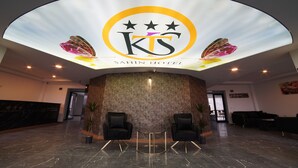 A hotel reception area with a modern design, featuring a curved ceiling with a logo, two black armchairs, a reception desk, and a marble floor. - ŞAHİN TERMAL OTEL VE SPA (Kutahya)