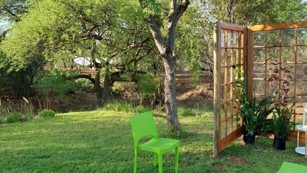 Zona d'estar a l'exterior amb un separador de fusta, dues cadires verdes i un llum.