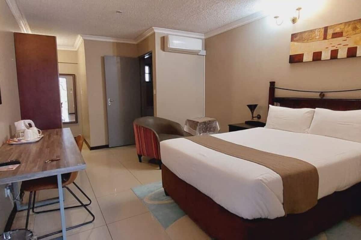 Habitación de hotel con cama, escritorio, silla, televisor y un cuadro en la pared.