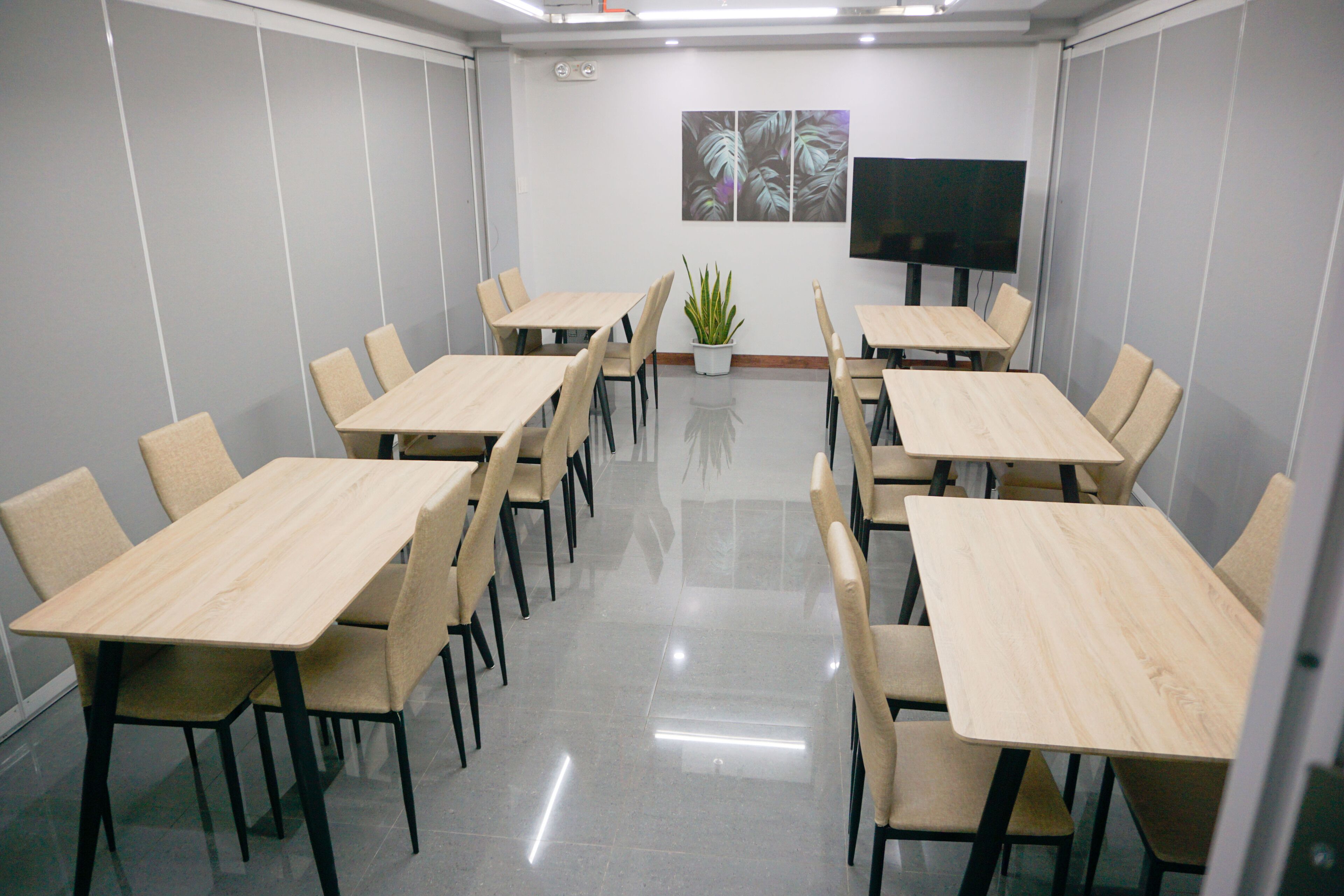 A conference room with multiple tables and chairs, a flat-screen TV, and a potted plant.