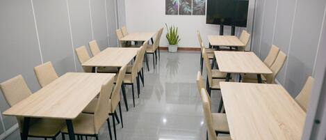 A conference room with multiple tables and chairs, a flat-screen TV, and a potted plant.