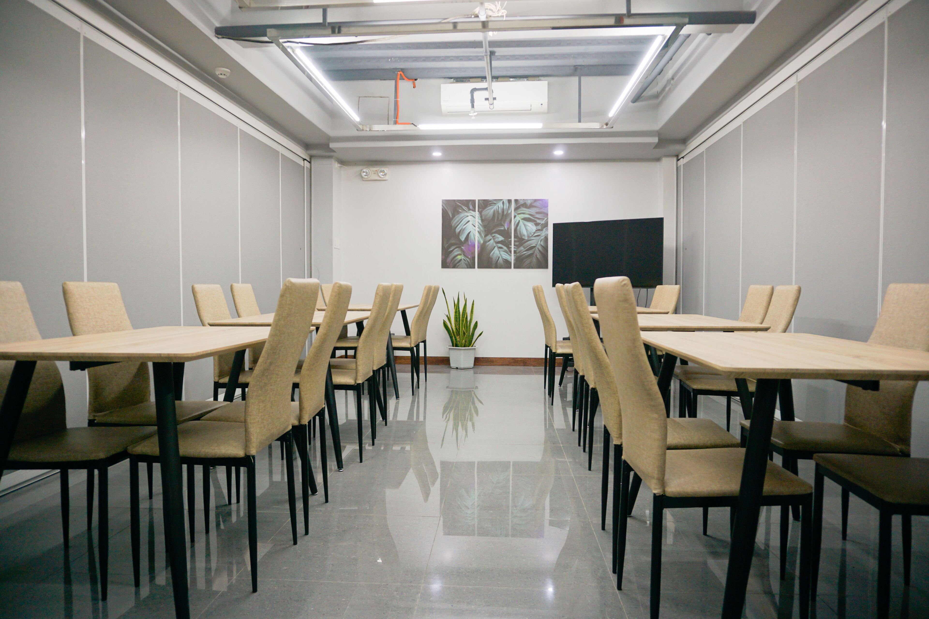 Un salón de conferencias con una mesa larga, varias sillas, una planta en maceta y un televisor de pantalla plana en la pared.
