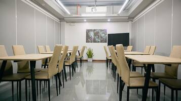 Un salón de conferencias con una mesa larga, varias sillas, una planta en maceta y un televisor de pantalla plana en la pared.
