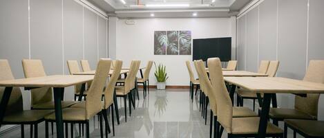 Un salón de conferencias con una mesa larga, varias sillas, una planta en maceta y un televisor de pantalla plana en la pared.
