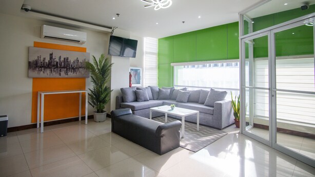 A modern living room with a grey sectional sofa, a white coffee table, and a potted plant. - Benrose Hotel (Cagayan de Oro)