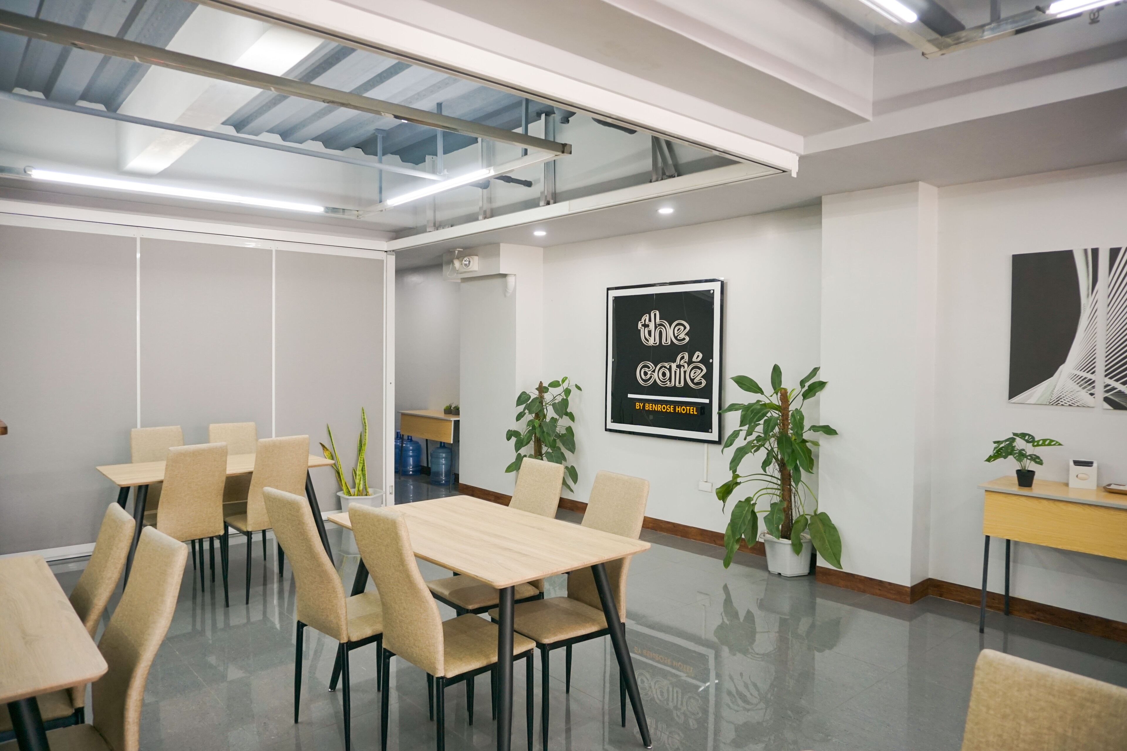 Una sala de conferencias moderna con techo de vidrio, sillas color beige, una mesa de madera y plantas en macetas.