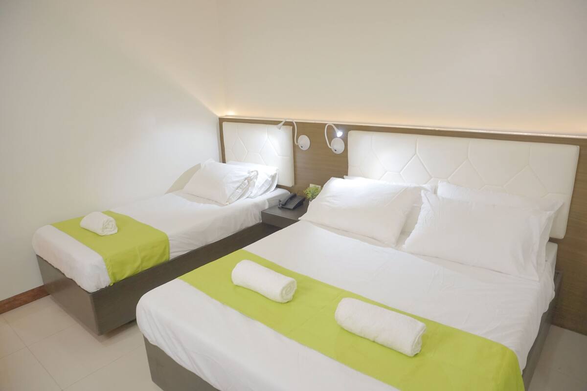 A hotel room with two beds, each with white linens and green bedspreads. There is a nightstand with a phone and a lamp between the beds.