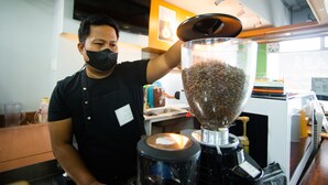 A person operating a coffee grinder in a kitchen area with a microwave and a sink in the background. - Benrose Hotel (Cagayan de Oro)