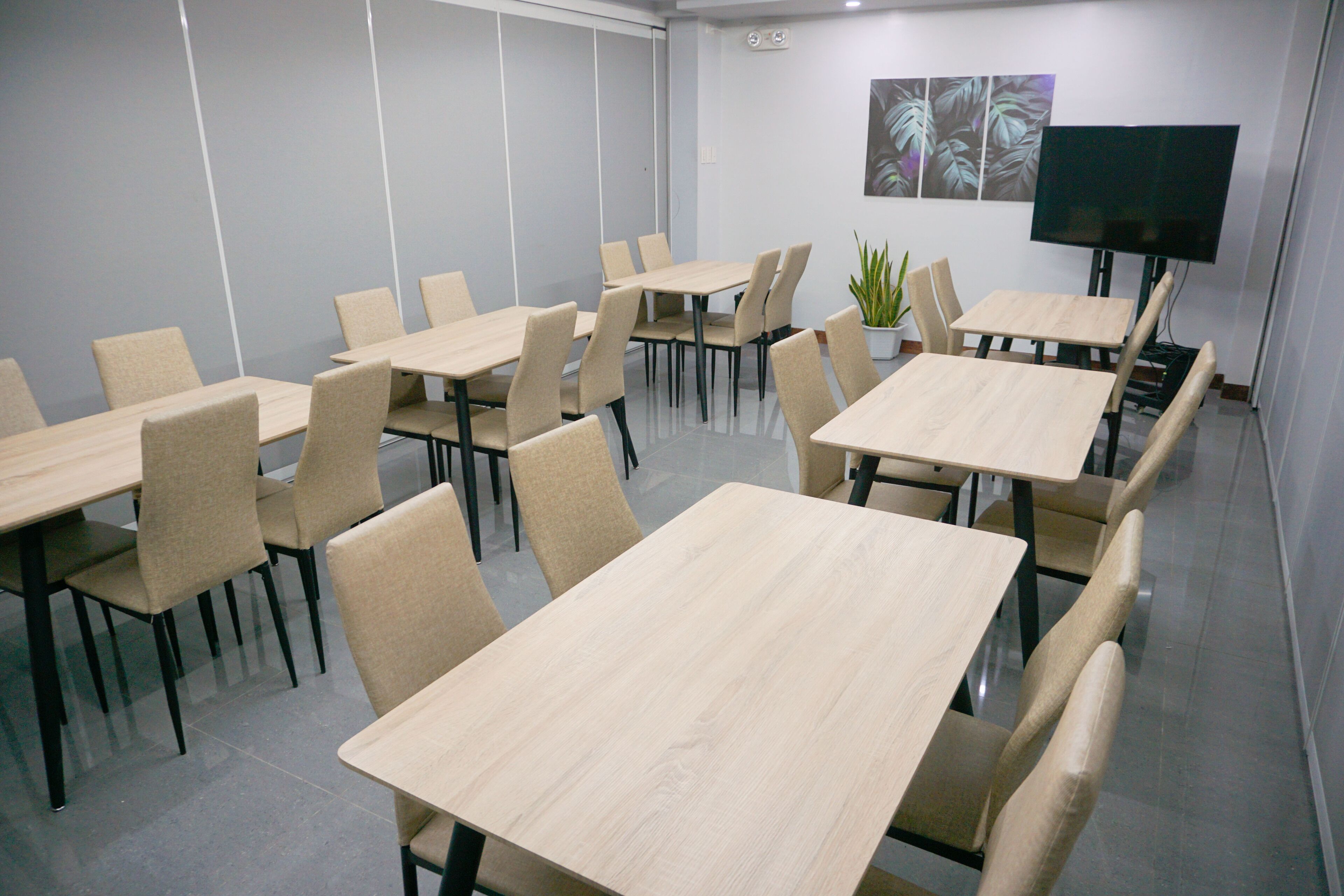 Une salle de conférence équipée de plusieurs tables et chaises, d’une plante en pot et d’un téléviseur à écran plat fixé au mur.