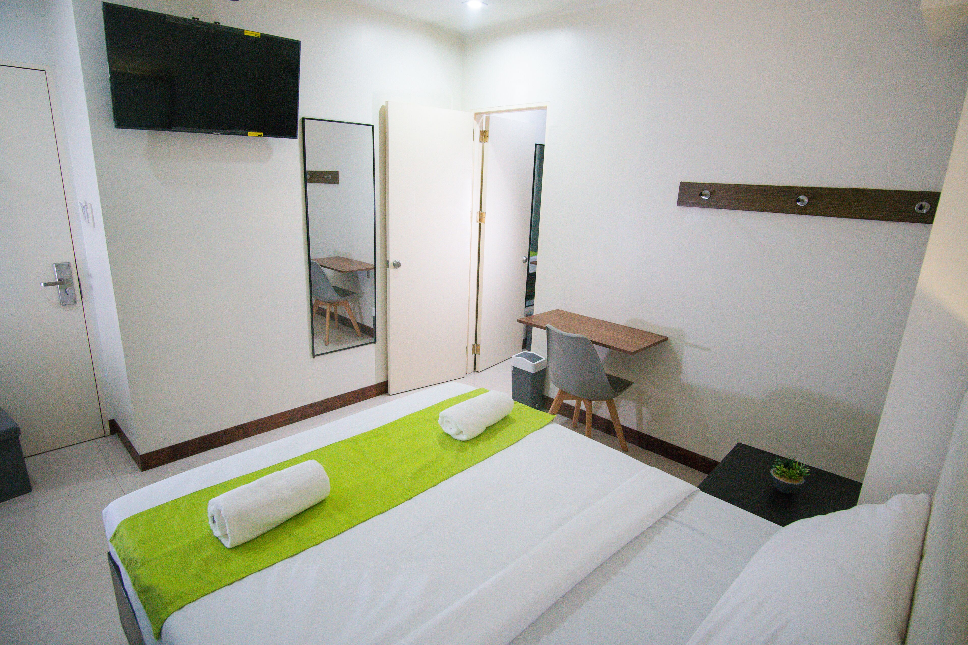 A hotel room with a bed, a desk, a chair, a TV, and a mirror.