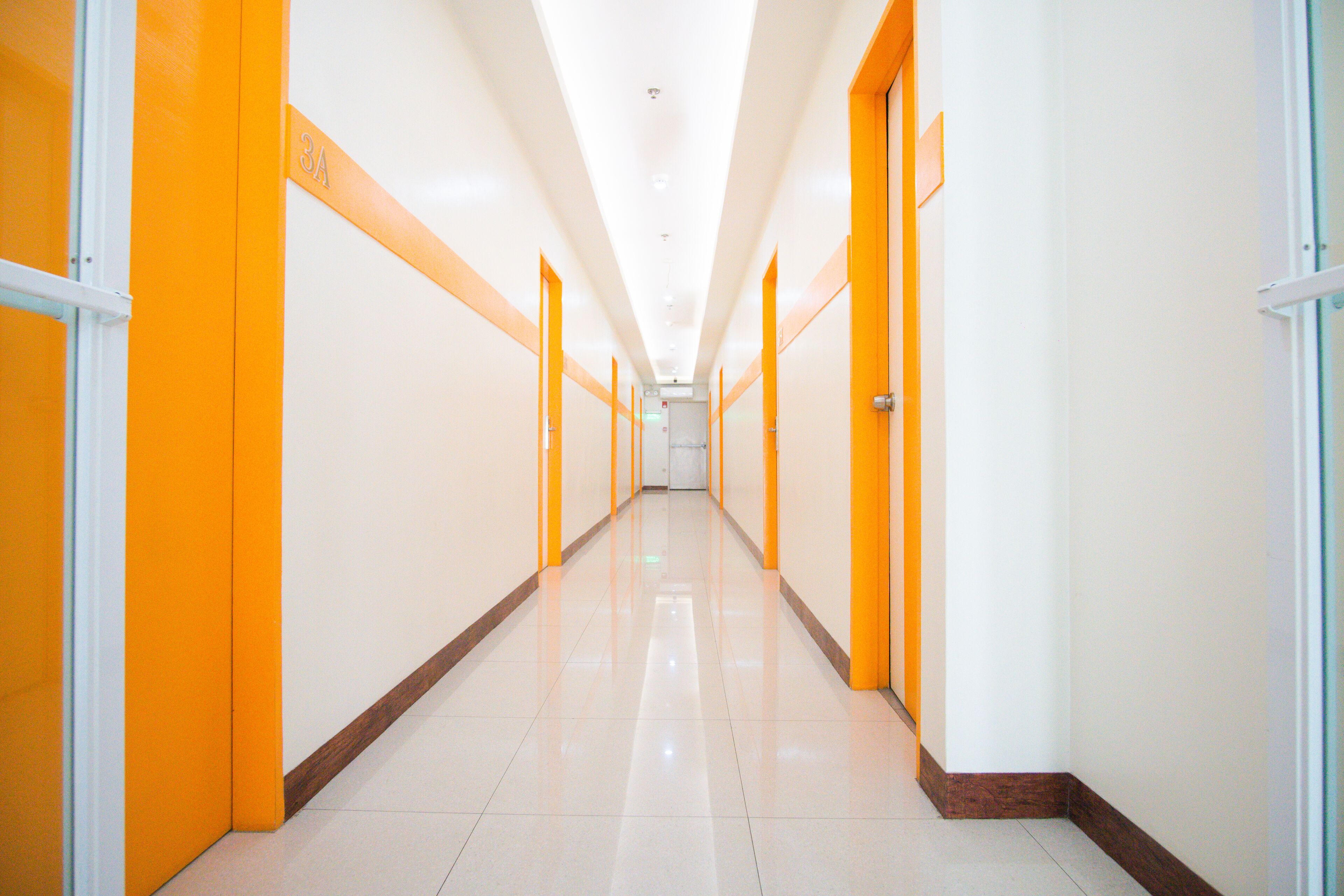 A long, brightly lit corridor with orange doors and white walls, leading to a door at the end.