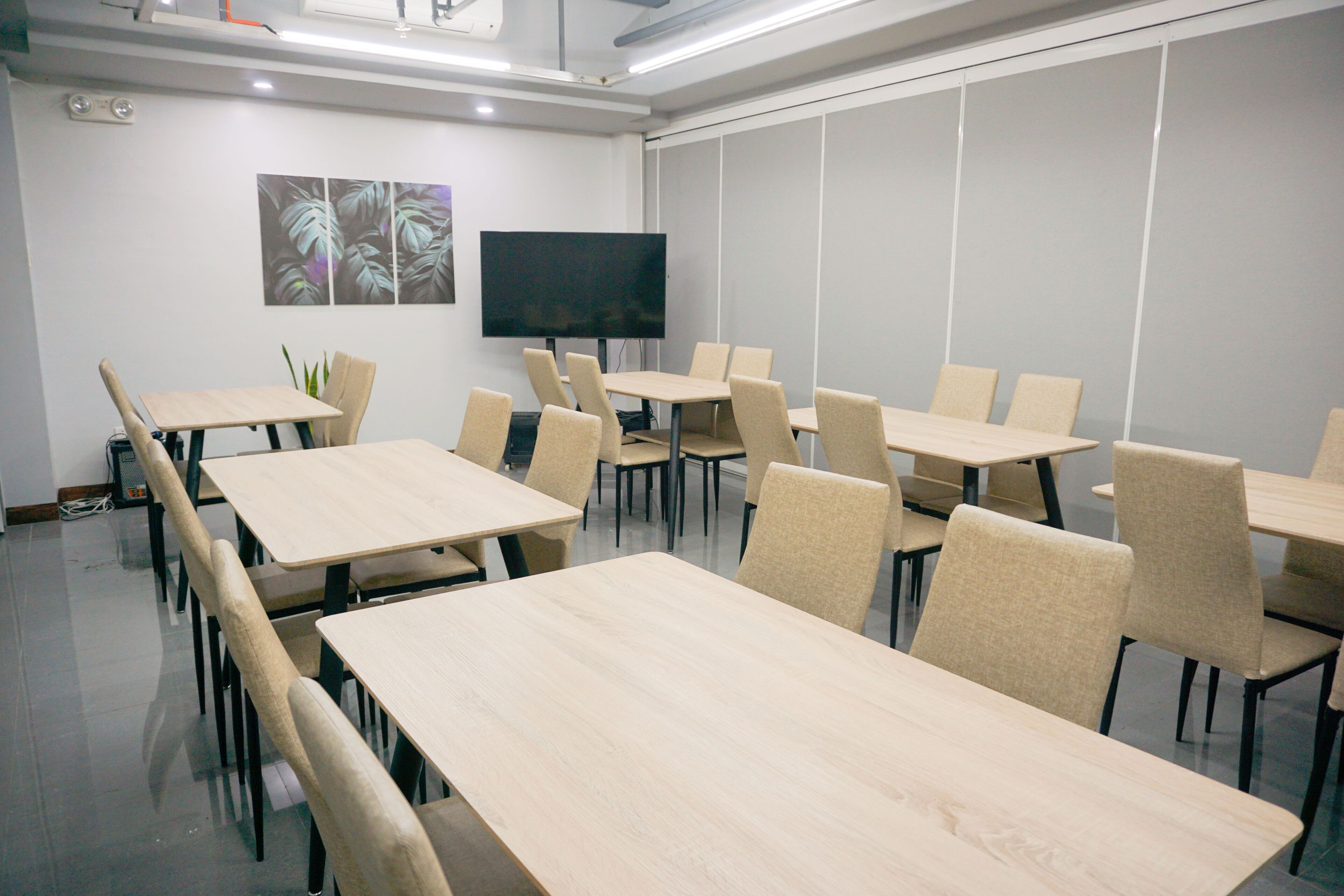 A conference room with multiple tables and chairs, a flat-screen TV, and a plant on the wall.