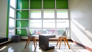 A modern room with a large window, two white chairs, a dark table, and a small stool. - Benrose Hotel (Cagayan de Oro)