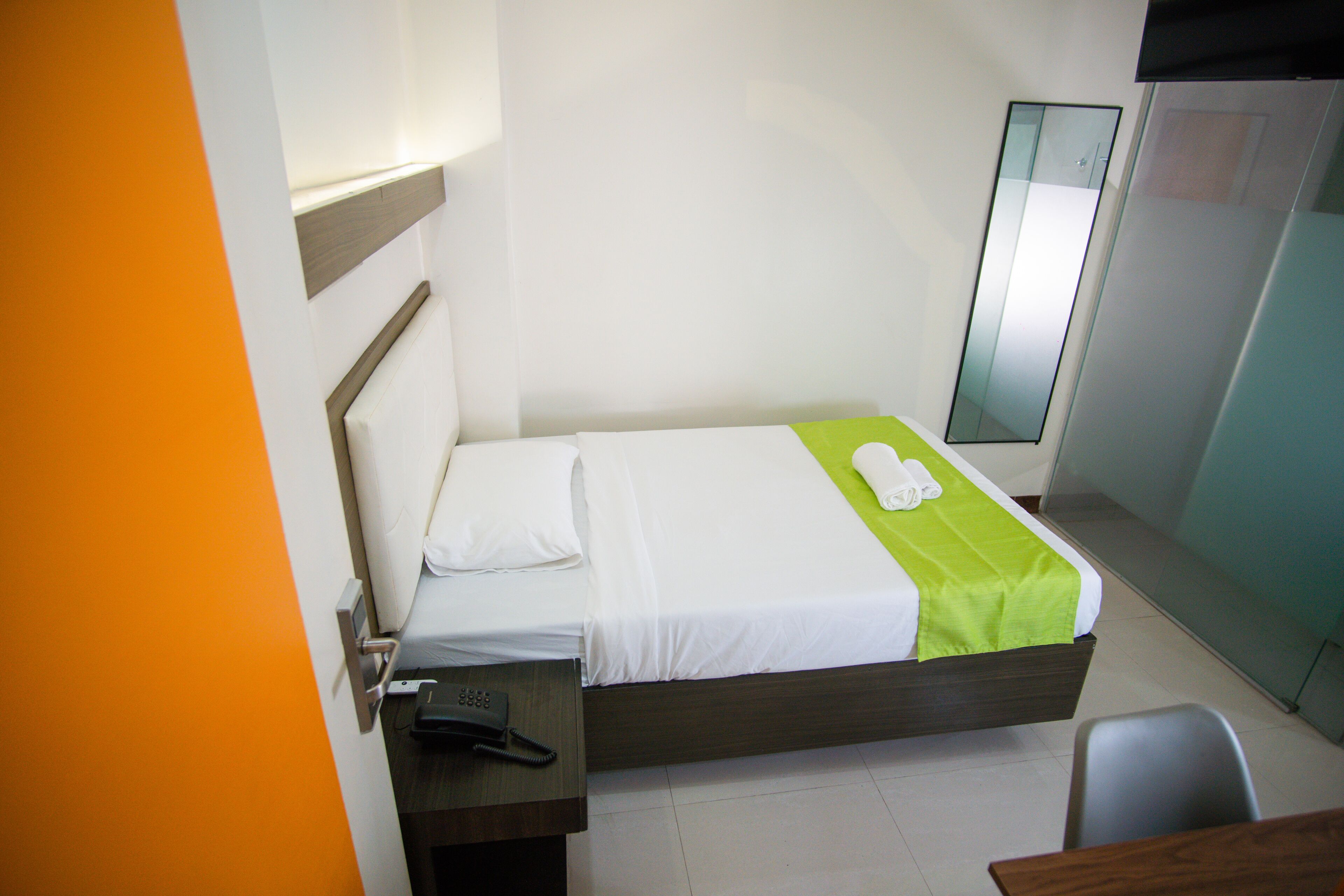 A hotel room with a bed, a desk with a telephone, and a chair.