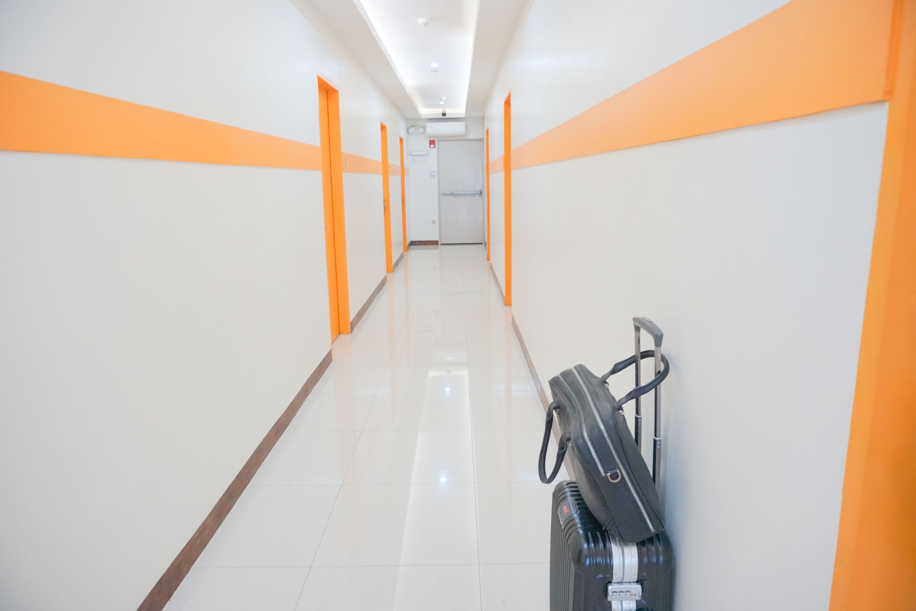 Een hotelgang met oranje accenten op de muren en een koffer aan de rechterkant.