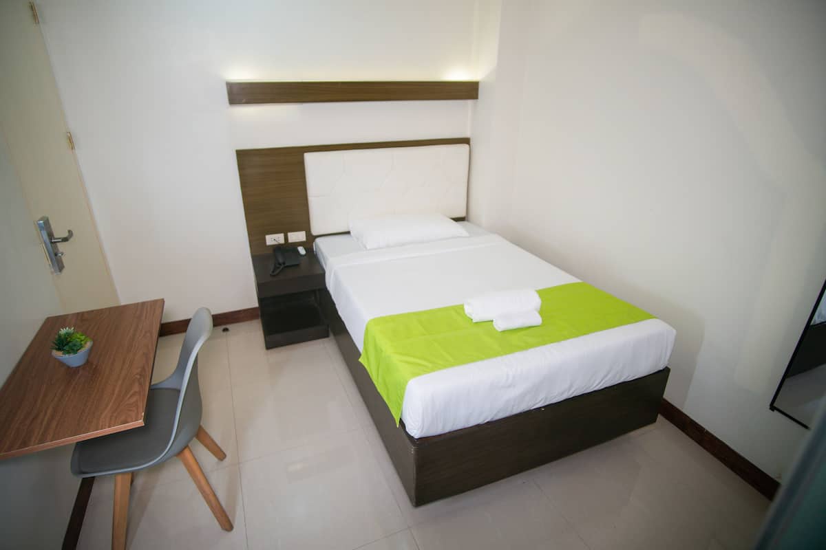 A hotel room with a bed, bedside table, chair, and a small table with a plant.