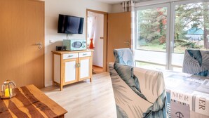 Quarto com armário de madeira, televisão, cama com roupa de cama floral e janela com vista para árvores e uma casa.