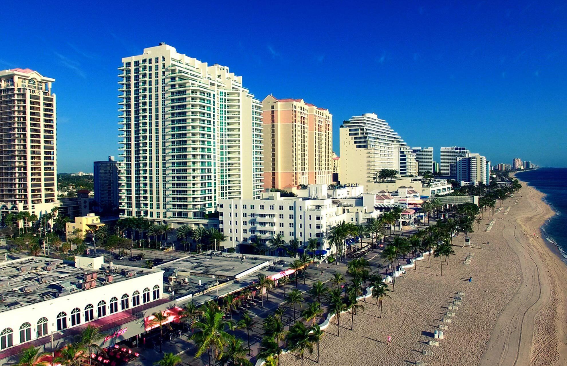 A coastal cityscape with high-rise buildings, a beach, and palm trees.
