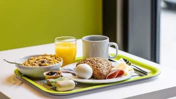 A breakfast tray with cereal, eggs, toast, and a glass of orange juice on a white table with a green tray.