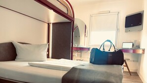 Ein Hotelzimmer mit Bett, Schreibtisch mit Computer, Fernseher und Fenster.