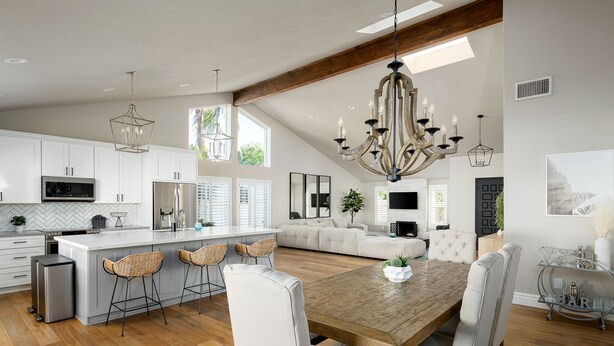 Una cocina amplia con una isla grande, muebles blancos y electrodomésticos modernos. Cuenta con una zona de comedor con mesa de madera y sillas blancas.