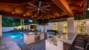 Cocina exterior con piscina, zona de bar y asientos.