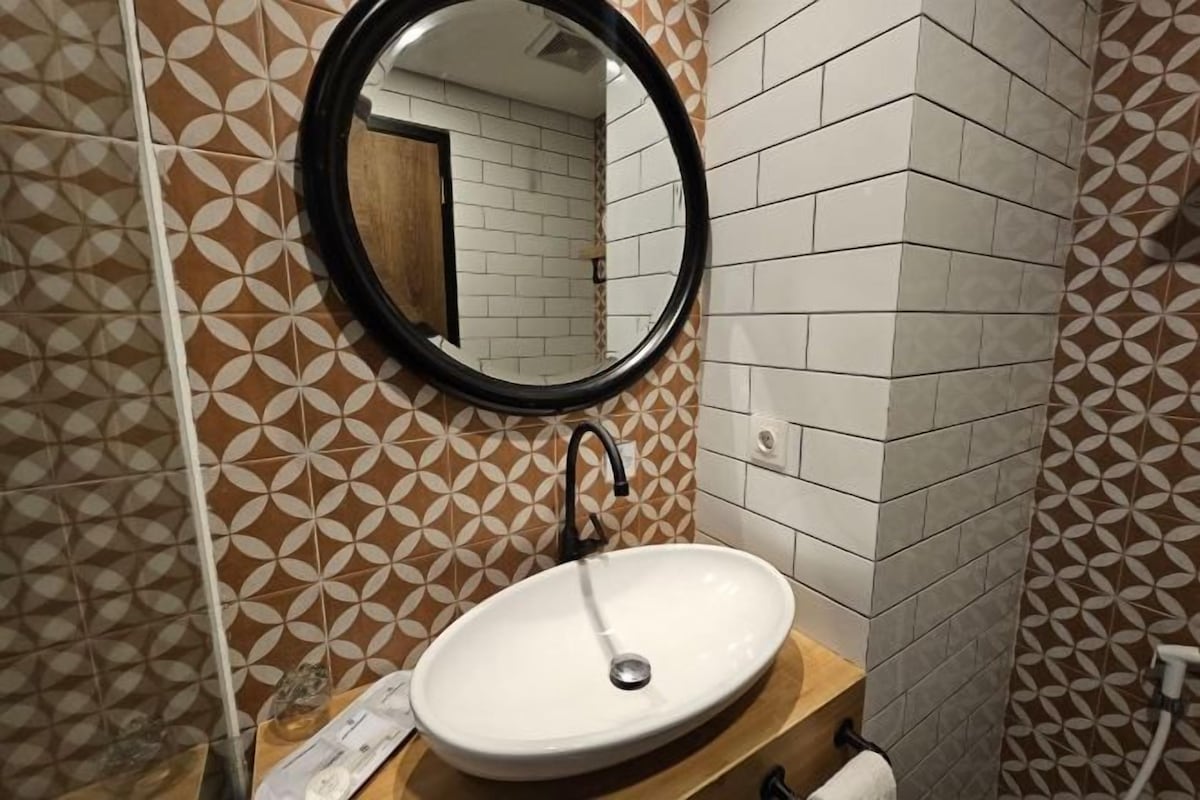 A bathroom with patterned tiles, a round mirror, and a white sink.