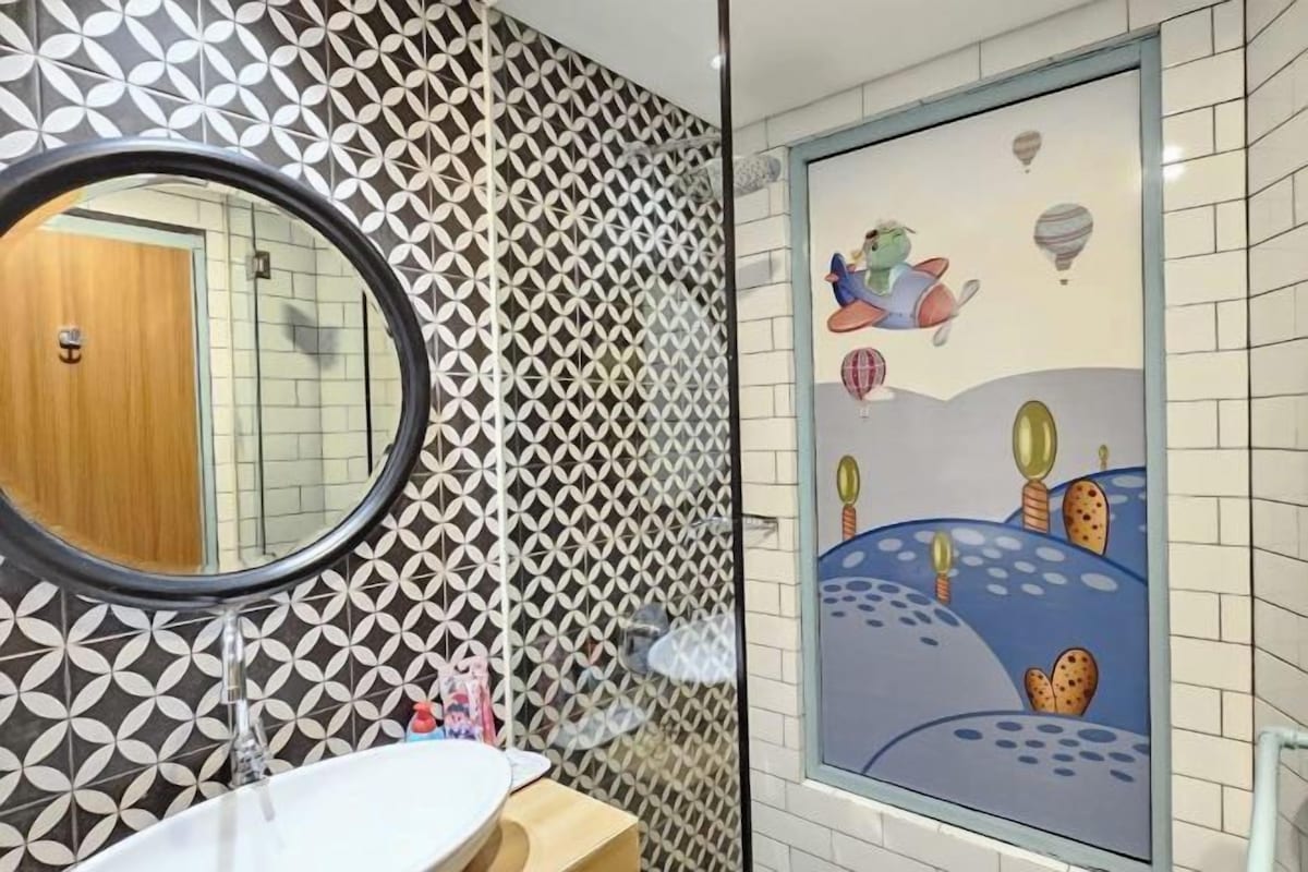 A bathroom with a geometric tile pattern, a round mirror, and a wall mural depicting a whimsical scene with hot air balloons and a character.