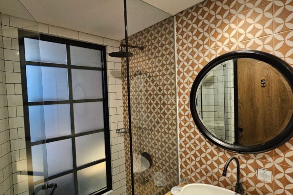 Un baño con cabina de ducha de vidrio, un espejo redondo y azulejos decorativos en la pared.