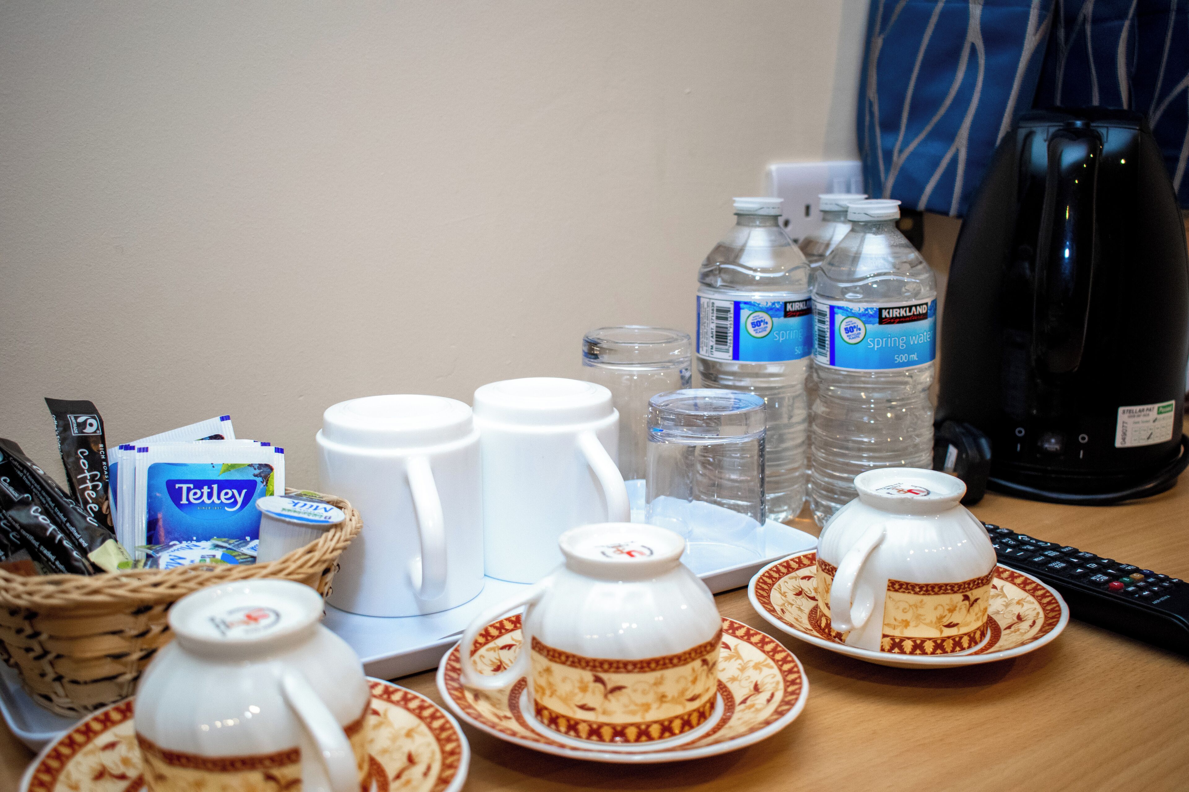 Una mesa dispuesta con tazas de té, botellas de agua, una cafetera y una cesta con sobres de café.