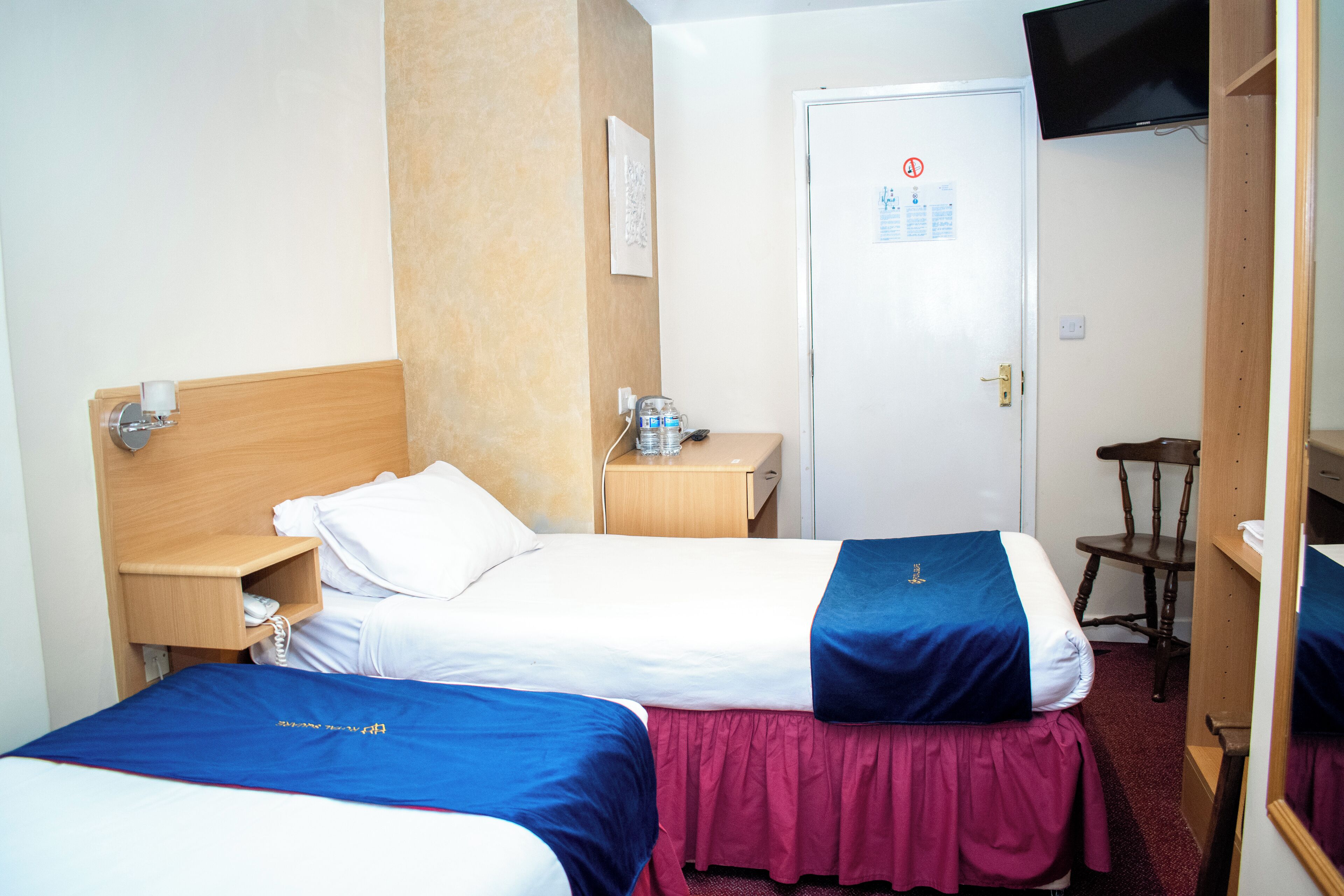 Camera d'albergo con due letti, una testiera in legno, un comodino, una sedia, un televisore e una porta con un cartello.