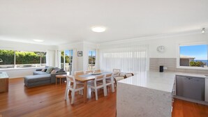 A modern, open-plan living space with a dining area, kitchen, and seating area. - MOON GLOW | Accom Holidays (TERRIGAL)