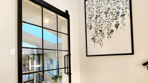 Ein modernes Interieur mit einer Glastür, die auf einen Balkon führt, einem gerahmten Pflanzenkunstwerk an der Wand und Holzböden.