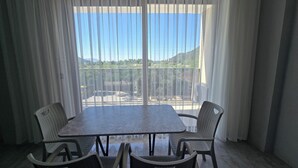 A balcony with a table and chairs, a view of a landscape, and a building in the distance. - OLIVE TREE APART HOTEL (Koycegiz)