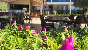 An outdoor seating area with tables and chairs, a covered patio, and a view of a building in the background. - OLIVE TREE APART HOTEL (Koycegiz)