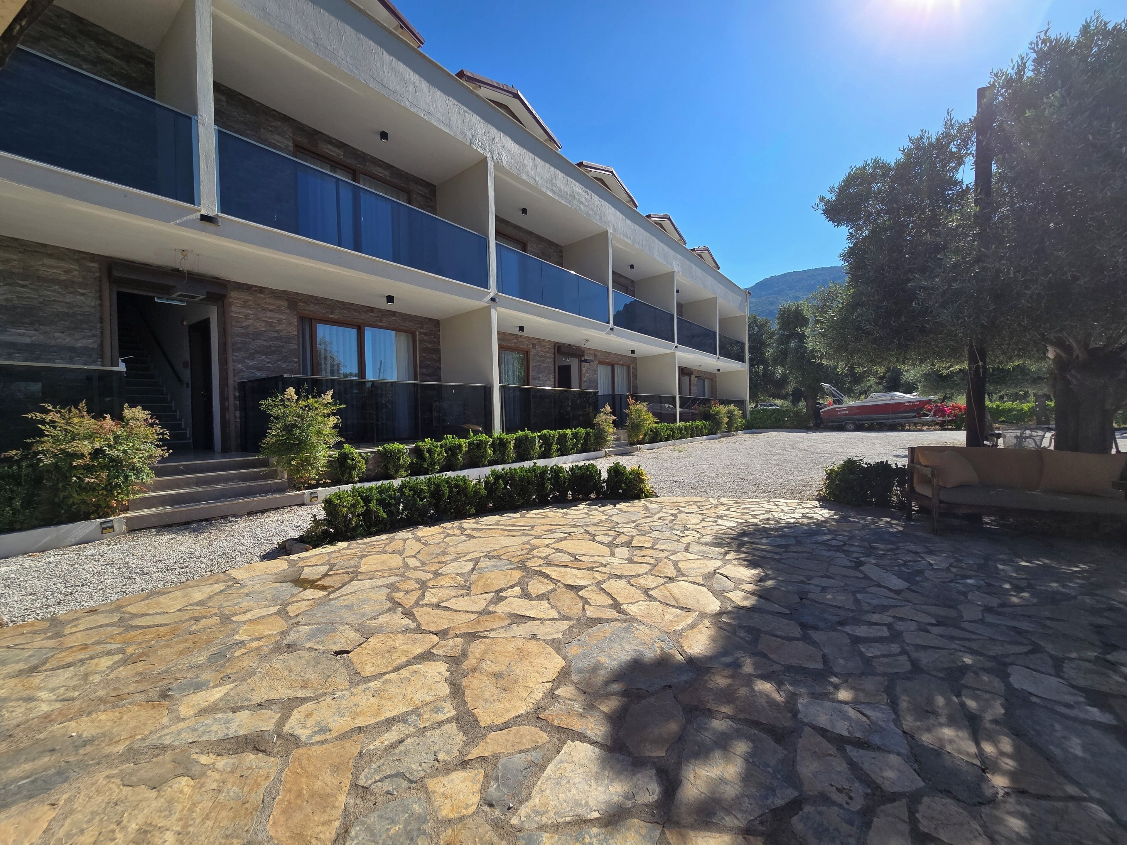 A multi-story hotel with balconies, a stone-paved courtyard, and a boat in the background.