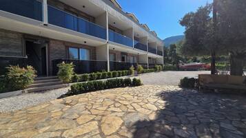 A multi-story hotel with balconies, a stone-paved courtyard, and a boat in the background.
