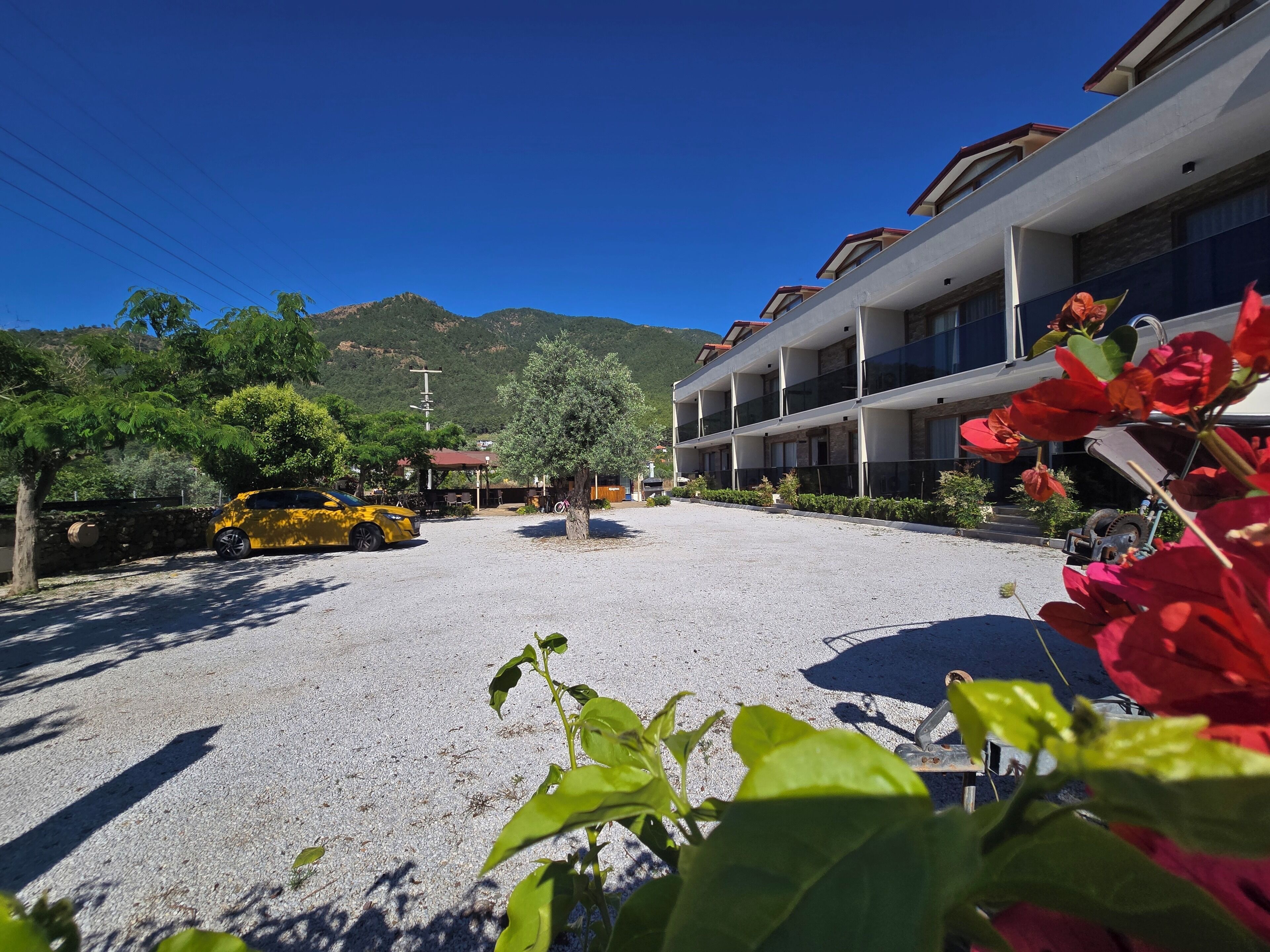 Un hôtel avec une allée gravillonnée, une voiture jaune garée devant et une montagne en arrière-plan.
