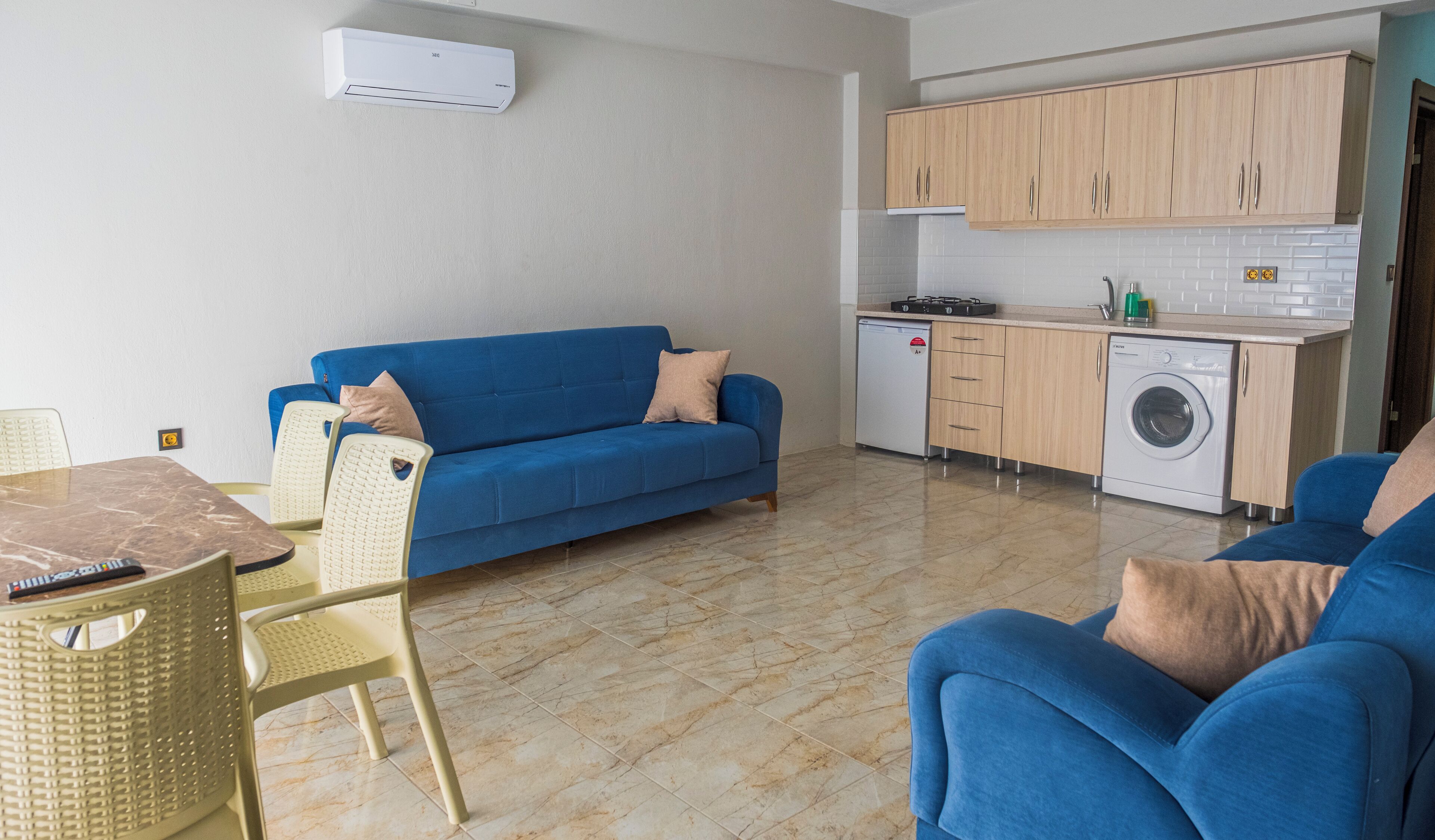Un espacio habitable compacto con sofá, mesa de comedor, lavadora y kitchenette.