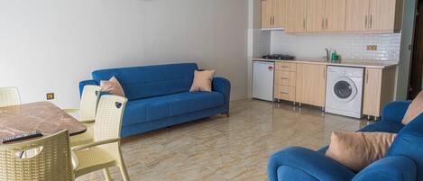 Un espacio habitable compacto con sofá, mesa de comedor, lavadora y kitchenette.