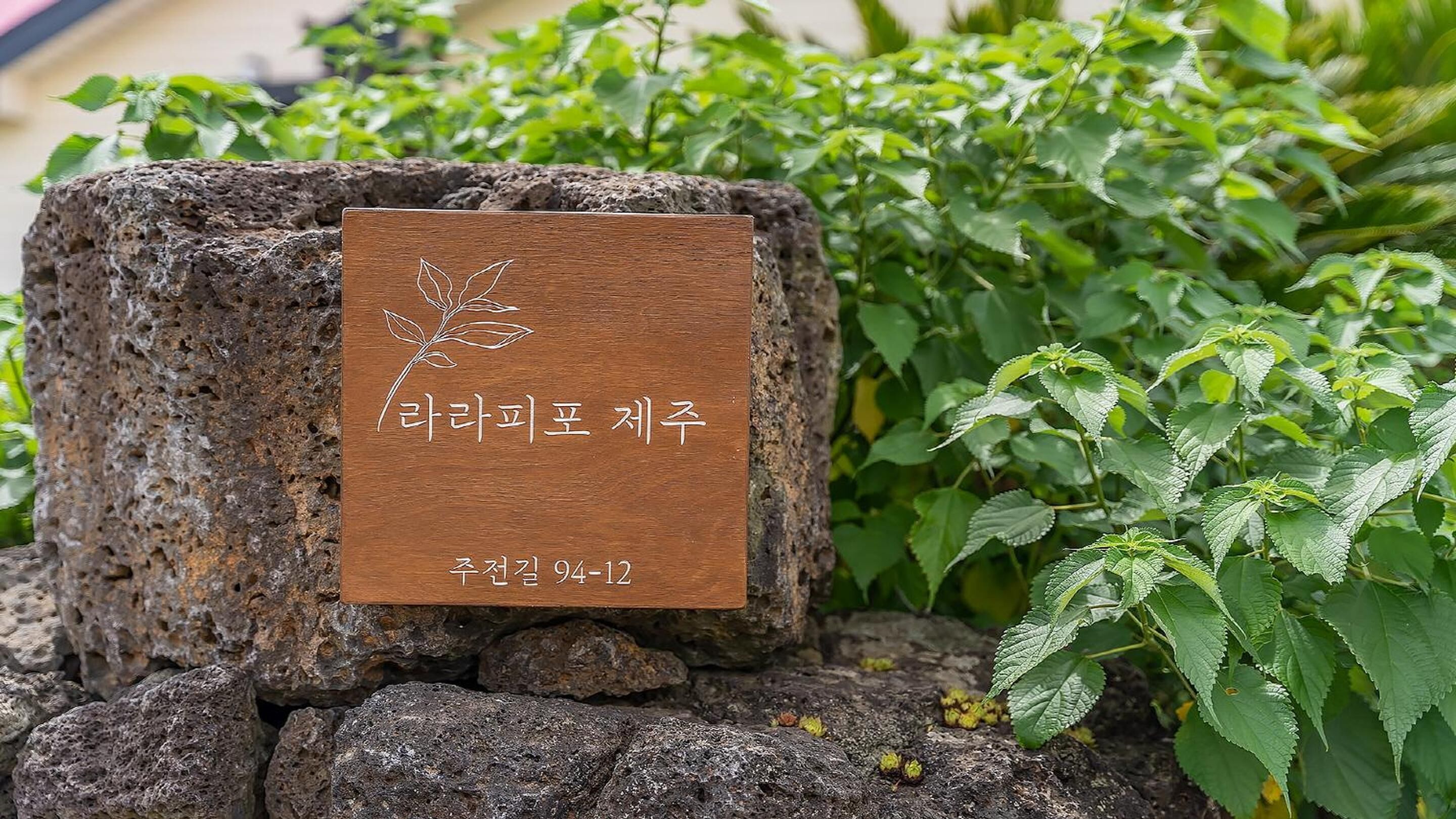 Une plaque en bois portant un texte en coréen et ornée d’un motif de feuille, fixée sur un rocher.