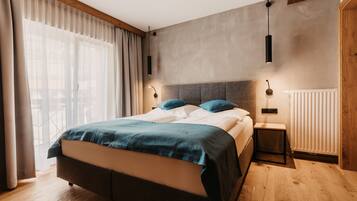 Een moderne slaapkamer met een groot bed, houten vloeren en uitzicht op de omgeving door dunne gordijnen.