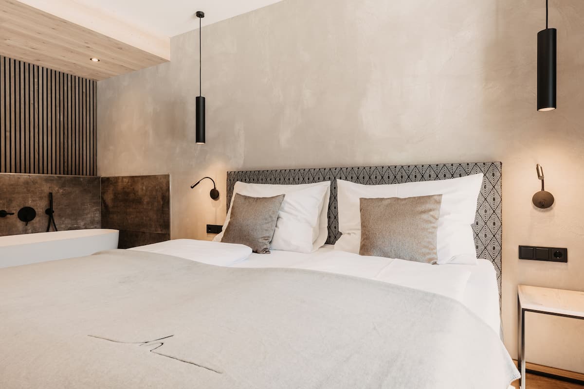 A modern bedroom with a large bed, a wooden slatted wall, and pendant lighting.