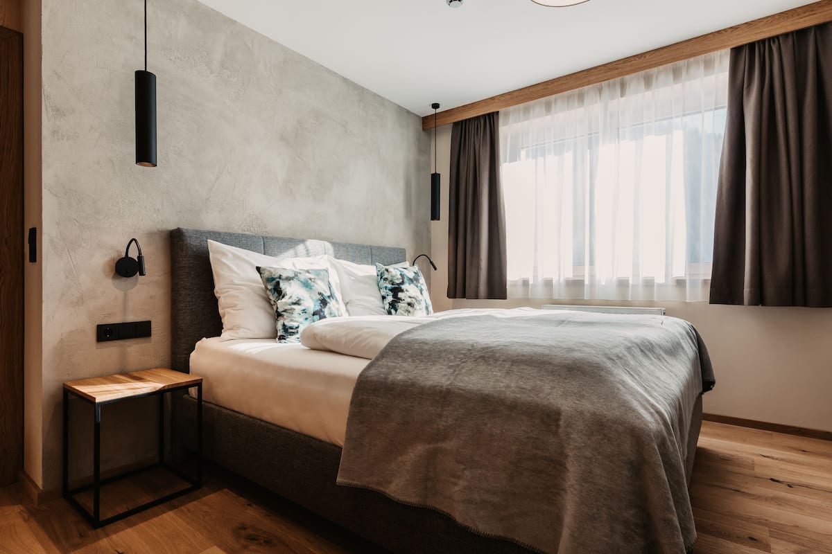A modern bedroom with a bed, a bedside table, a hanging light, and a window with curtains.