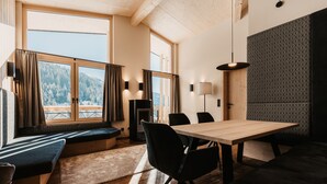 Una habitación acogedora con una mesa de madera, sillas negras, un banco y vistas a una montaña nevada a través de amplios ventanales.